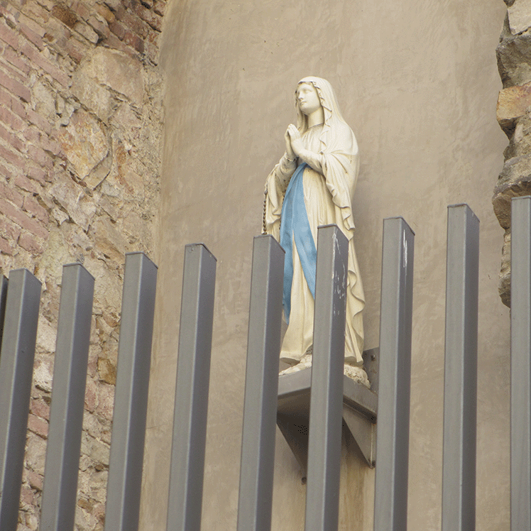 statue of virgin mary hanging on a wall behind a fence